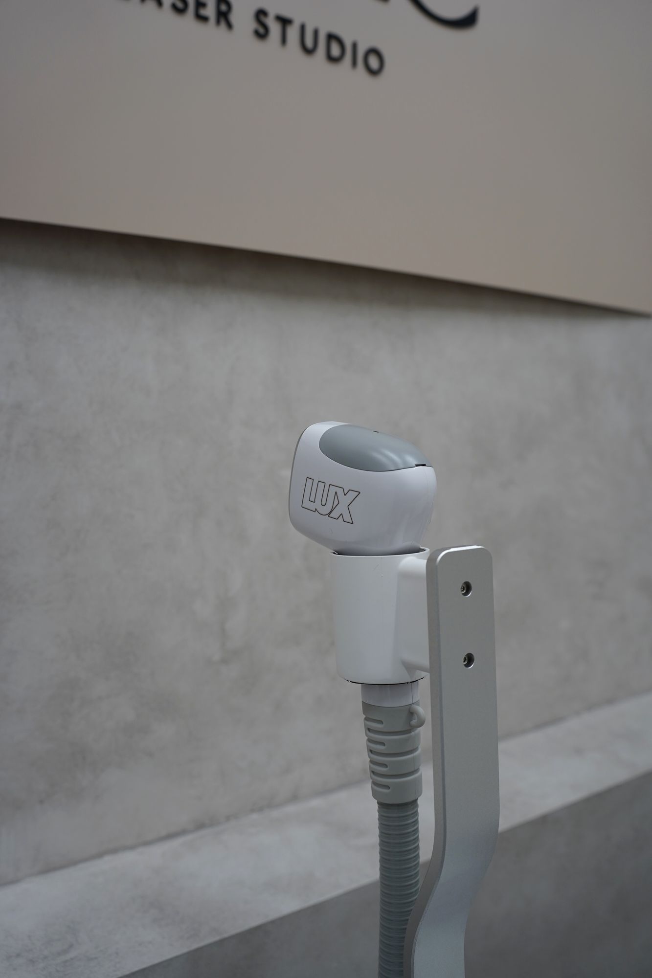 The laser handpiece in front of the Luxe Laser Studio sign